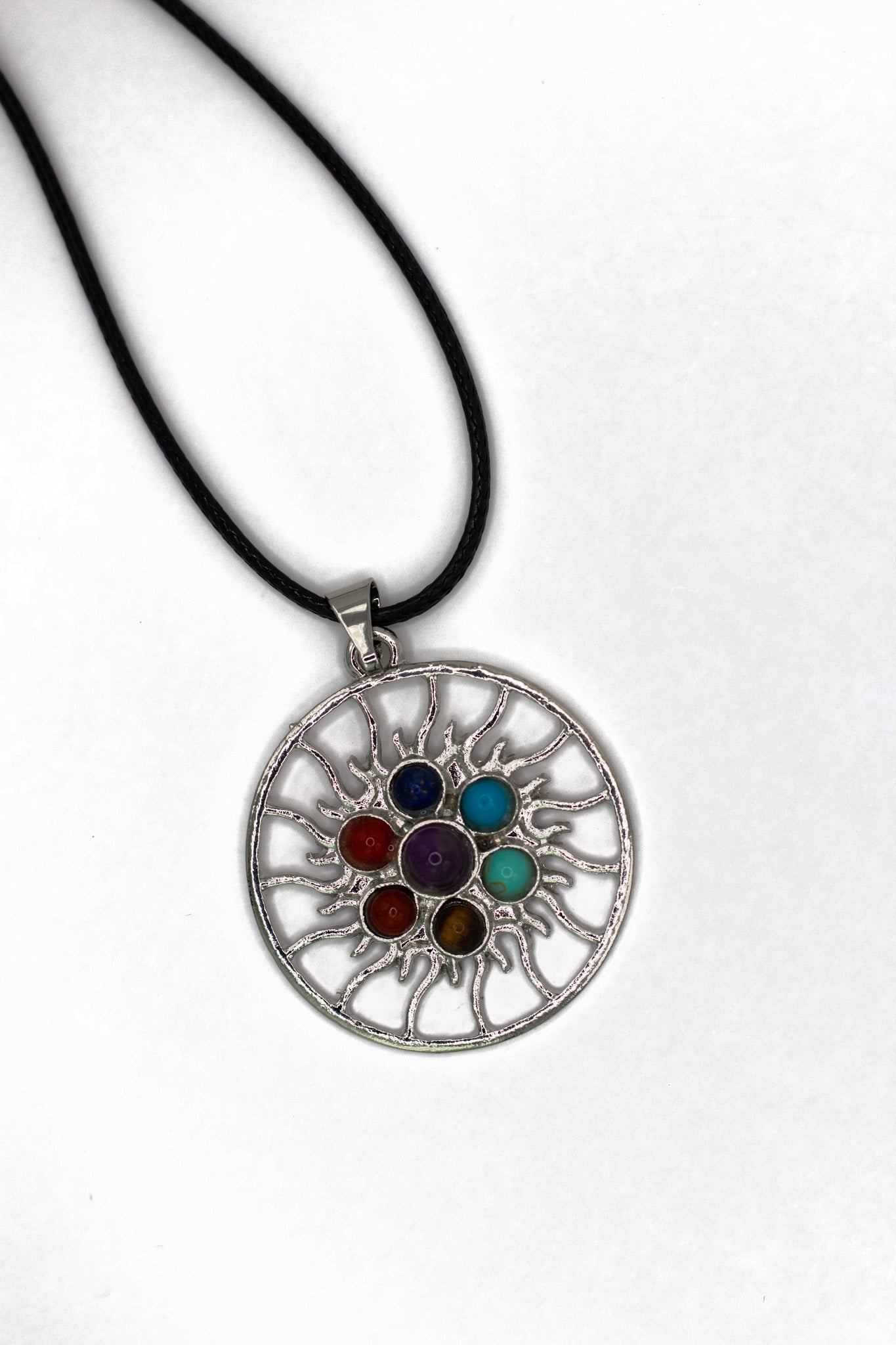 Chakra Anhänger Sonne aus rhodiniertem Metall mit 7 handgefertigten Edelsteinen, Ø ca. 45 mm, an geflochtener Baumwollkette mit Karabinerverschluss. Symbolisiert Harmonie und Ausgeglichenheit.